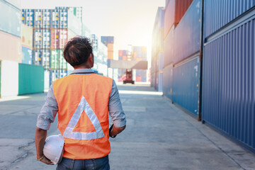 Rear view foreman checking and control loading container with walkie talkie radio and holding hard safety helmet. Architect standing and looking at container and forklift blurred background.