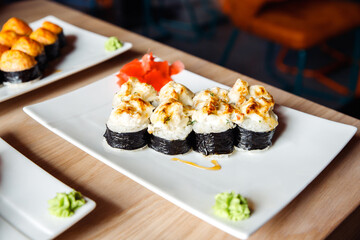 Baked Maki sushi, baked rolls on white rectangular plate. Chicken, rice, nori seaweed, cream cheese, cucumber, gouda cheese, unagi sauce, herbs. Front view. Selective focus.