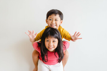 Cute Sibling sister and brother asian Korean Thai portrait kids.Asian children boy child siblings riding the back his sister on white wall at home.fun family.homeschool kid brother sister.hormones kid - Powered by Adobe