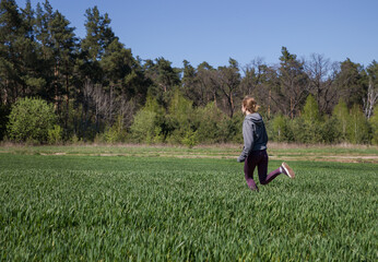 Naklejka na ściany i meble young slender teenager girl is jogging cross-country. Active lifestyle. Healthy workouts. Young woman running through the meadow