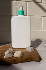 white bottle with dispenser for cosmetic product on wooden stand with natural stones in hard daylight