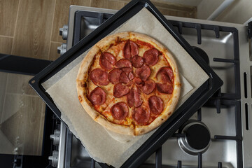 freshly baked pizza on a baking sheet and baking paper. a baking sheet with pizza is on the stove