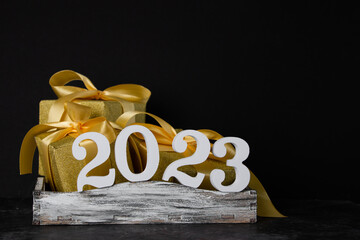 Gift boxes in golden packaging and white numbers 2023 on a black background. Holiday concept.