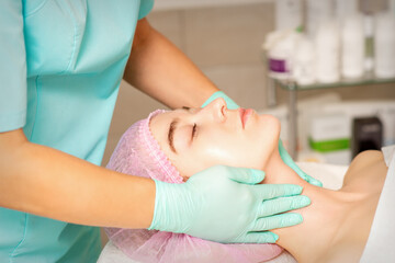 Naklejka premium Cosmetologist with gloved hands applies a moisturizing mask with peeling cream on the female face. Facial cosmetology treatment. Procedures for facial care