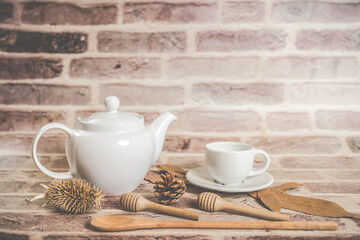 Tea concept, white teapot with white tea cup with dry leaves on wooden background.