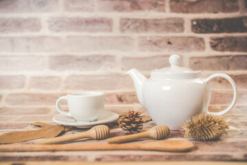 Tea concept, white teapot with white tea cup with dry leaves on wooden background.