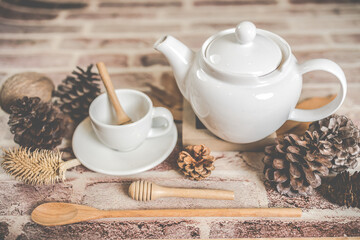 Tea concept, white teapot with white tea cup with dry leaves on wooden background.