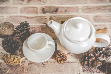 Tea concept, white teapot with white tea cup with dry leaves on wooden background.