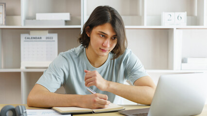 Distance education concept, Teen boy taking notes while studying online with teacher on video call