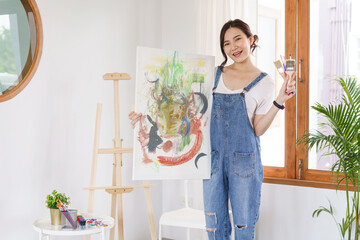 Creative of art concept, Young asian woman holding artwork and paint brush after drawing finish