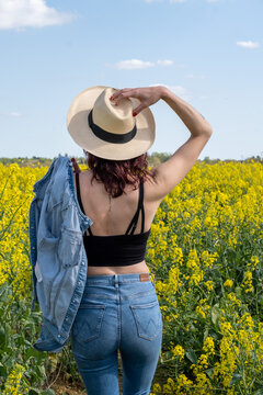 Rear view of a woman standing in a rapeseed field in spring with her hand on her head, France