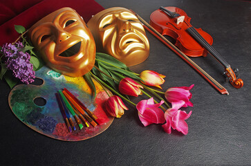  Attributes of the arts. Music, painting, theater. Violin, art palette, brushes, theatrical masks and a bouquet of tulips. On a black background.