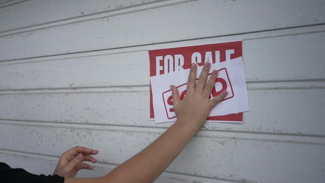 Female hand putting Sold sign on For sale advertisement in slow motion. Unrecognizable Caucasian woman selling garage. Property sale and purchase concept