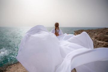 Happy freedom woman on the beach enjoying and posing in white dress. Rear view of a girl in a fluttering white dress in the wind. Holidays, holidays at sea.