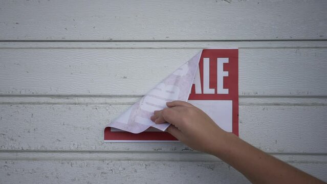 Female hand tearing off Sale sign from white garage door in slow motion. Unrecognizable Caucasian woman buying house with carport. Property ownership concept