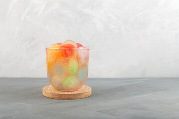 Rainbow cocktail. Refreshing summer drink with fruits ice. Multicolored soft drink. Grey background, copy space