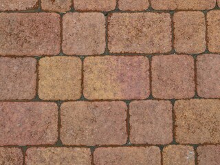 a fragment of a stone pavement top view full frame, granite rounded cobblestones in the structure of a street paved surface, a red-brown stone background with a grainy aged texture