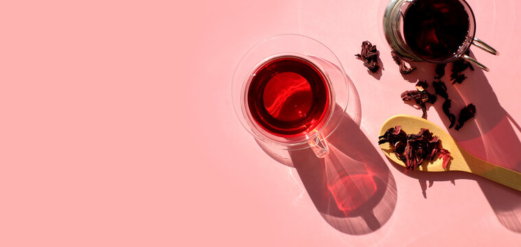 Tea cup of hibiscus tea and teapot on pink background, top view. Light and shadow. Banner with copy space