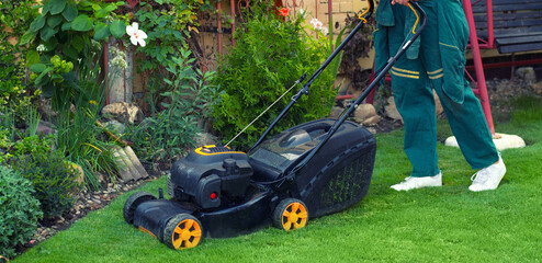 Fototapeta premium Young gardener mowing the lawn with lawnmower in summer