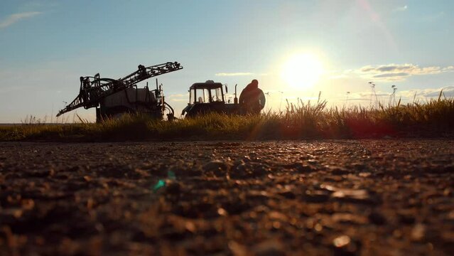 Farmer at Dusk. Silhouette young farmer in tractor preparing land with seedbed cultivator at sunset time. Male farmer walking in sunny field. Silhouette agricultural harvest farming by tractor.