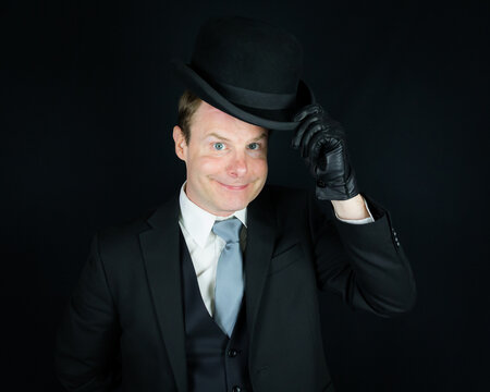 Portrait of British Businessman in Dark Suit Tipping a Bowler Hat in Polite Greeting. Vintage Style and Retro Fashion of Eccentric English Gentleman.