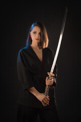 Portrait of a young brunette kung fu girl with a Japanese sword on a black background.