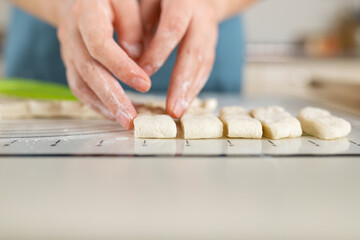 Close-up of floured hands spreading even pieces of dough along the markings on a kitchen baking mat.