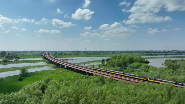 Train driving over the Hanzeboog train bridge over the river IJssel near the city of Zwolle in Overijssel during a springtime day. Aerial drone point of view.