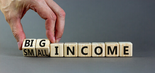 Big or small income symbol. Businessman turns wooden cubes and changes words Small income to Big income. Beautiful grey table grey background, copy space. Business big or small income concept.