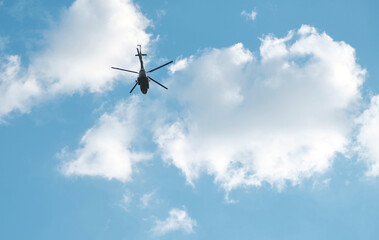 Fototapeta na wymiar High, silhouette of helicopter flying high against blue sky with white clouds. Bottom view.