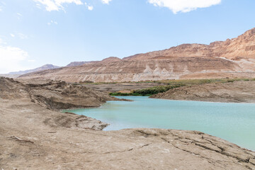 Fototapeta na wymiar Sinkhole filled with turquoise water, near Dead Sea coastline. Hole formed when underground salt is dissolved by freshwater intrusion, due to continuing sea-level drop. . High quality photo