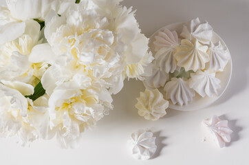 Bouquet of white peonies on a white background and white meringue cookies.