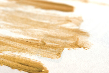Gold metallic streaking of makeup on white background.