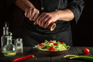 The chef adds peppers to a fresh vegetable salad in a kitchen. Close-up of chef hands holding a mill. Cooking healthy and tasty food