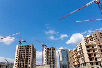 Construction site with multi-storey residential buildings under construction. Tower cranes in action on blue sky background.