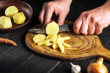 Professional chef cuts raw potatoes into small pieces with a knife. Close-up of a chef hands while working in kitchen. Cooking delicious breakfast or dinner.