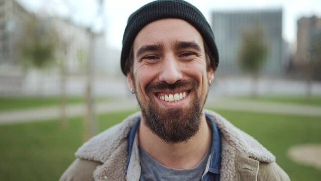 Cheerful bearded man wearing hat looking at the camera outdoors