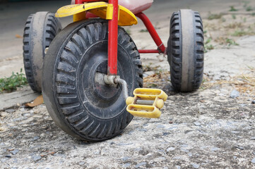 close up wheel of old tricycle on dirty concrete ground
