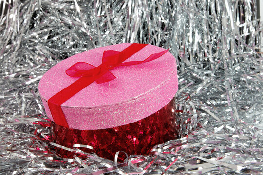 Pink and red Valentine gift box with red bow in a bed of silver foil streamers.