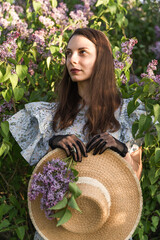Dreamy caucasian young woman looking up, in retro clothes with boatman's straw hat in a blooming lilac garden.