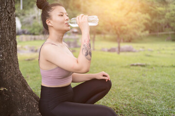Young beautiful woman drinking water after exercise in park