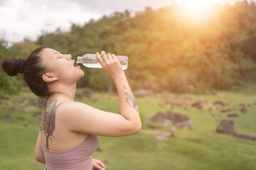 Young beautiful woman drinking water after exercise in park