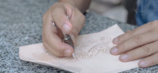 Closeup Leather craftsman using tool engraving patterns on genuine leather in leather workshop