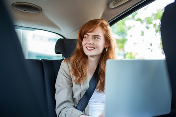 Fototapeta na wymiar Pensive businesswoman with laptop in back seat of car. Young woman using a laptop in a car.