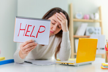 A frustrated female freelancer is tired of working at home, holds a notebook with the inscription 'Help'