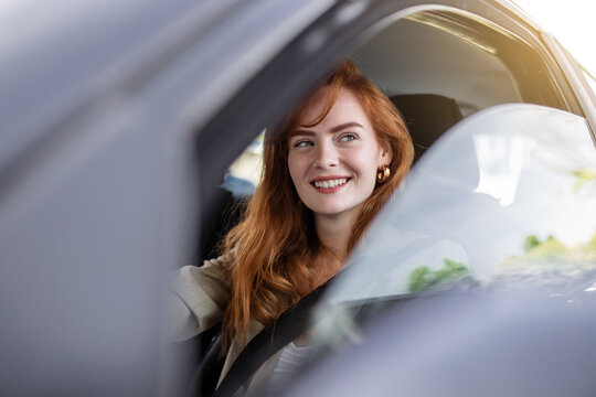 Cute young lady happy driving car. Image of beautiful young woman driving a car and smiling. Portrait of happy female driver steering car with safety belt