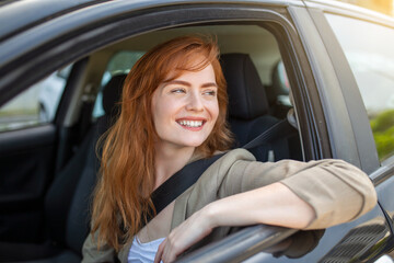 Beautiful young woman driving her new car at sunset. Woman in car. Close up portrait of pleasant looking female with glad positive expression, woman in casual wear driving a car - obrazy, fototapety, plakaty