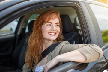 Foto op Canvas Beautiful young woman driving her new car at sunset. Woman in car. Close up portrait of pleasant looking female with glad positive expression, woman in casual wear driving a car © Graphicroyalty