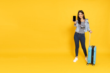 Happy Asian woman traveler standing and showing screen of smartphone isolated on yellow background, Tourist girl having cheerful holiday trip concept, Full body composition
