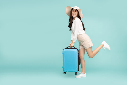 Happy Asia woman traveler standing and holding suitcase isolated on green background, Tourist girl having cheerful holiday trip concept, Full body composition
